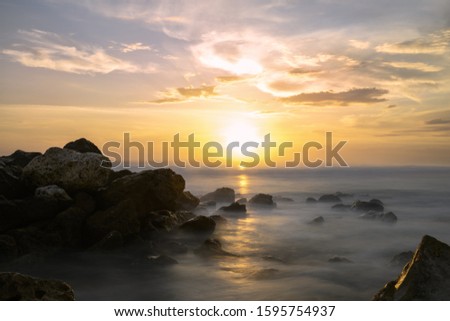 (Selective focus) Stunning long exposure picture of a rocky coast bathed by a smooth silky sea during a beautiful and dramatic sunset. Melasti Beach, South Bali, Indonesia.