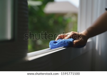Hand holding blue microfiber cloth for cleaning dust on the glass window rail Royalty-Free Stock Photo #1595771500
