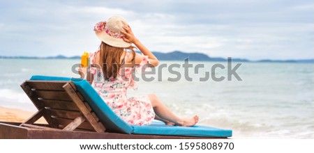 Summer beach holiday concept. Young asian woman relax on beach hold orange refreshment cocktail with floppy hat in pink dress. Clear sky background banner with copy space. Pattaya, Thailand