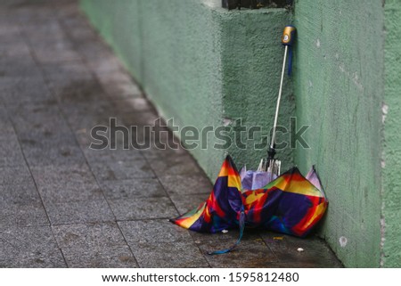 Close-up. A broken multi-colored umbrella lies against the wall of the building in windy rainy weather. Thrown out umbrella.