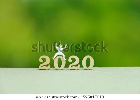 Miniature people - Clown seat on 2020 wooden number on a table with dreamy green background. Greeting for happy new year