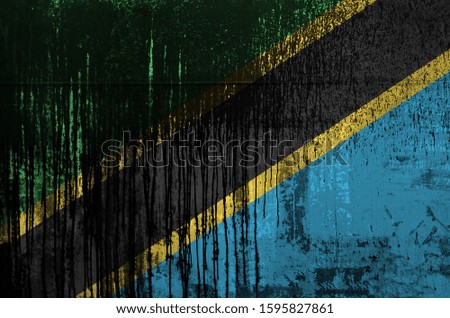 Tanzania flag depicted in paint colors on old and dirty oil barrel wall closeup. Textured banner on rough background