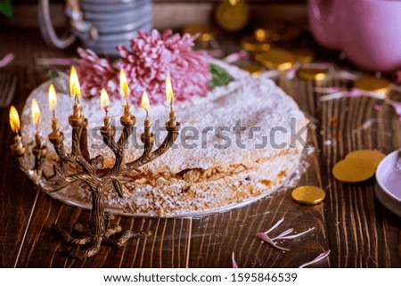Jewish menorah with burning candles and holiday cake decorated with flowers.