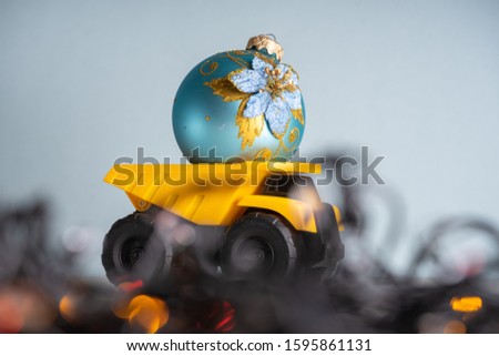 Yellow dump truck model with Christmas tree toy. Garland lights in defocus
