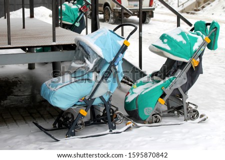 Two winter baby strollers in blue and turquoise color outdoors in snowy weather. Wheel sled. Stock photograpy.