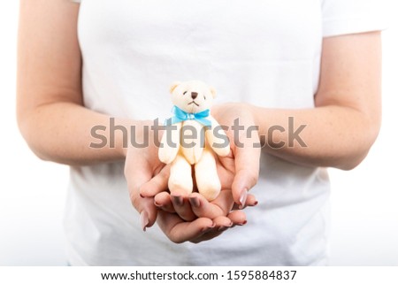 Woman's hands holding little smiling white teddy bear on lap for future baby. Homely atmosphere. Emotional loving moment in pregnancy