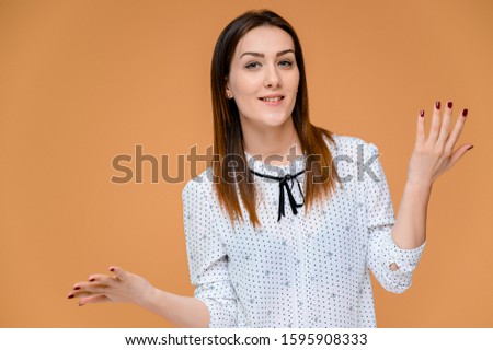 Secretary concept. Portrait of a pretty woman, manager in a white blouse with smooth dark hair. He is standing right in front of the camera, smiling, showing emotions on an orange background.