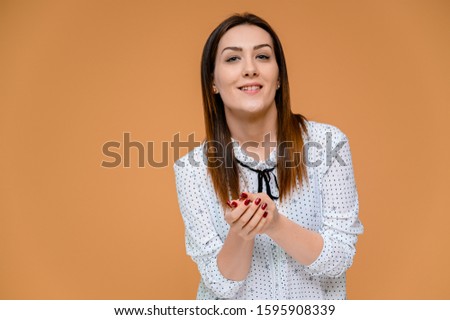 Secretary concept. Portrait of a pretty woman, manager in a white blouse with smooth dark hair. He is standing right in front of the camera, smiling, showing emotions on an orange background.