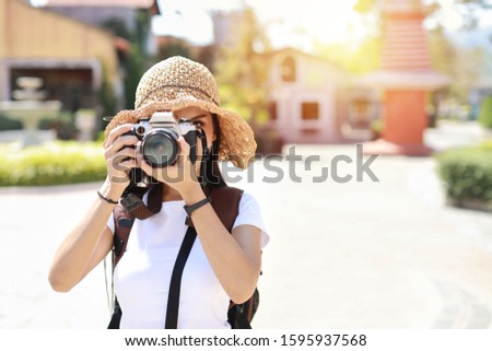 Portrait cute asian photographer girl cover her face with camera. Attractive beautiful traveller asian women in white shirt and hat with backpack having fun in Asia city outdoor summer time.  