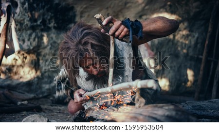 Close-up Shot of a Primeval Caveman Wearing Animal Skin Trying to make Fire with Bow Drill Method. Neanderthal Kindle First Man-Made fire in the Human Civilization History. Making Fire for Cooking. Royalty-Free Stock Photo #1595953504