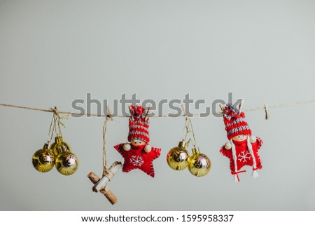 Red knitted christmas stars in funny hats. Christmas dolls and ornaments hanging on the rope with clothespin. Golden christmas balls on the rope