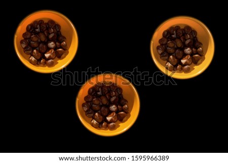 Three orange bowls full of horse-chestnuts prepared for making chetnut animals or feeding animals on black background