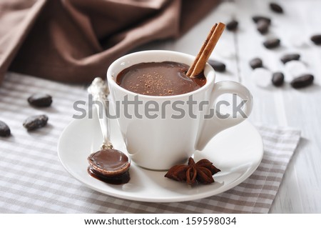Hot Chocolate in cup with cocoa powder and cinnamon stick on wooden background