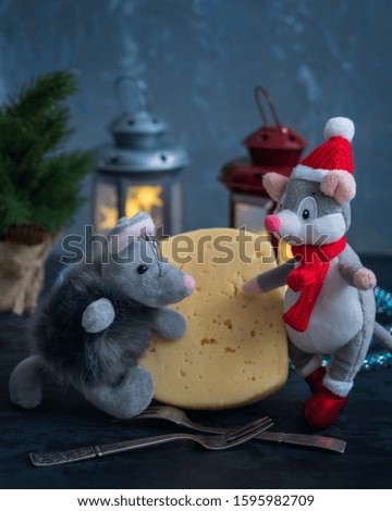 Christmas card with toys mice, symbols of the year and a large piece of cheese and forks on the background of burning lanterns