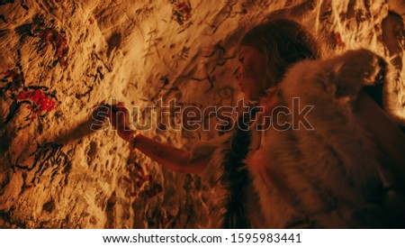 Primitive Prehistoric Neanderthal Child Wearing Animal Skin Draws Animals and Abstracts on the Walls at Night. Creating First Cave Art with Petroglyphs, Rock Paintings Illuminated by Fire. Low Angle
