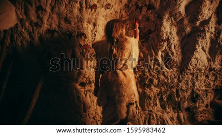 Back View of a Primitive Prehistoric Neanderthal Child Wearing Animal Skin Draws Animals and Abstracts on the Walls at Night. Creating First Cave Art with Petroglyphs, Rock Paintings.