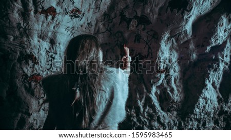 Back View of Primitive Prehistoric Neanderthal Child in Animal Skin Draws Animals and Abstracts on Walls. Creating First Cave Art with Petroglyphs, Rock Paintings. Shot Made at Night with Cold Light
