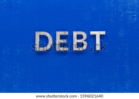 the word debt layed on blue painted board with thick silver metal aphabet characters
