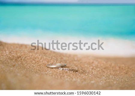 Two wedding white gold rings in the sand on the background of beach and sea. 