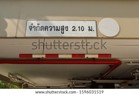 Closeup car height limit sign made from PVC pipe painted with red and white, hanging from ceiling by chains, the Thai language means limit height 2.10 m 