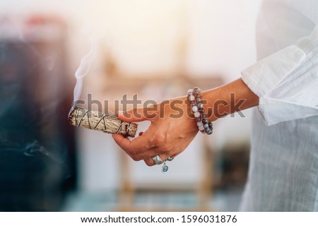 Smudging - Hands of a spiritual woman holding burning smoking sage smudge stick Royalty-Free Stock Photo #1596031876