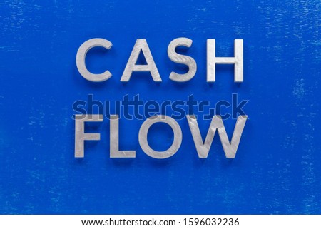 The words cash flow layed on blue painted board with thick silver metal aphabet characters.