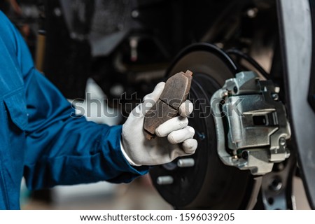 cropped view of mechanic holding brake pad near assembled disc brakes Royalty-Free Stock Photo #1596039205
