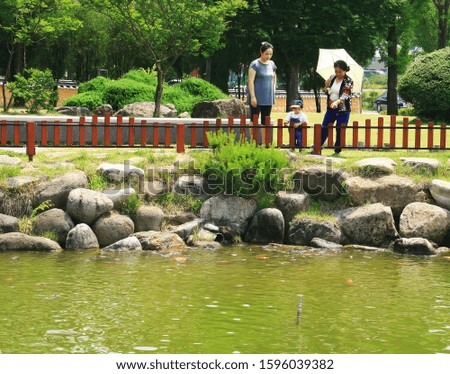 A picture of a grandmother, grandson, and wife watching a fish in a park pond.