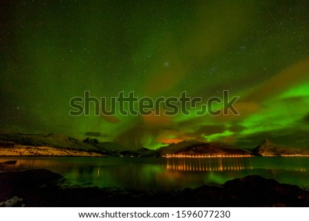 northern lights, Aurora borealis over fjord mountains with many stars on the cloudy sky in Lofoten islands, Norway, long shutter speed.