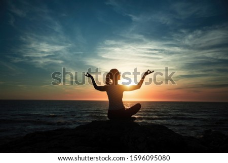 Silhouette of yoga woman meditating on the ocean beach during wonderful sunset.
