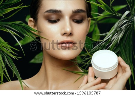 beautiful woman with bright make-up near the green leaves of bushes on nature and moisturizer
