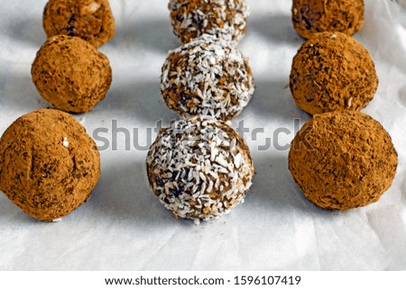 Raw food balls.Handmade vegan sweets made from almonds, walnuts, dates, raisins, coconut and cocoa. Raw food candies in coconut and cocoa close-up on white paper on a dark table laid out in rows. 