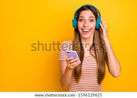 Photo of funny pretty lady hold telephone cool wireless earphones turn on radio listen love confession overjoyed wear casual striped t-shirt isolated yellow color background