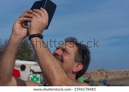 Caucasian man makes selfie with mobile phone. Camera on a beach.