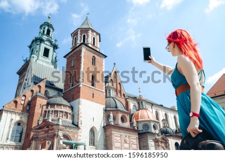Woman taking picture, selfie on smartphone, standing on the street near the Wavel castle in Krakow, Poland. Tourism travel concept, copy space. Summer day. sunglasses, smartphone in hand.
