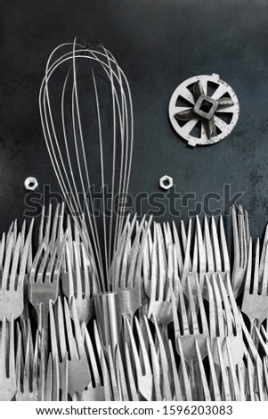 Whisk for whipping lies on an old wall in the middle of a sea of ​​forks. The design idea has transformed the subject of making it wonderful, fanastastic as from wonderland. Revived subject with eyes.
