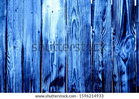 Fragment of burnt and wet old grey wooden fence with rusted screws, knots and openings between planks as a trendy blue background. Main trend of 2020.