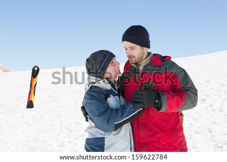 Happy loving couple with ski board on snow in background against clear blue sky