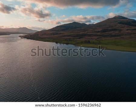 A picture of Loch Vennachar in Scottland at sunset with the colours reflecting in the water. The lake is surrounded by small mountains typical for the Highlands. 