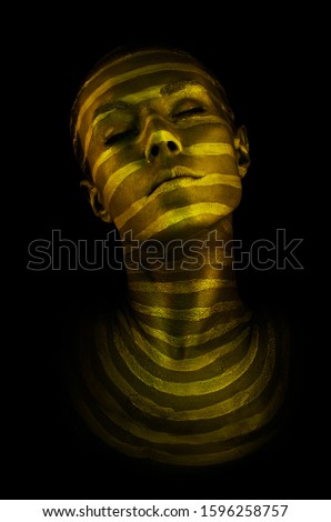Portrait of a young woman with original creative golden glowing make-up. Model with dark and light lines, drawn on the face. Isolated on black background. 