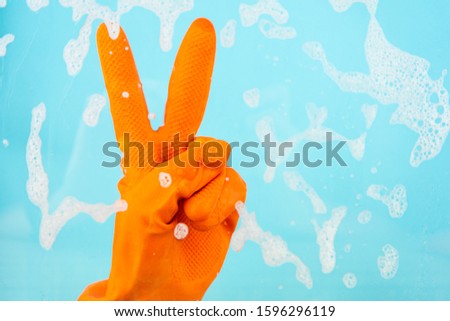 Showing two fingers on a blue background while wearing orange gloves, the cleaning concept.
