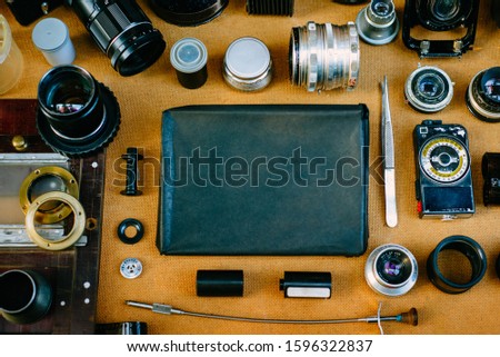 Retro mockup, retro black pack for photo paper in center and vintage photographic accessories and quipments around on Wooden Background. Top view