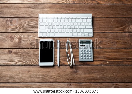 Top view of accountant workspace with office accessories. Flat lay wooden desk with computer keyboard, calculator and smartphone. Accounting and banking services. Finance and investment concept.