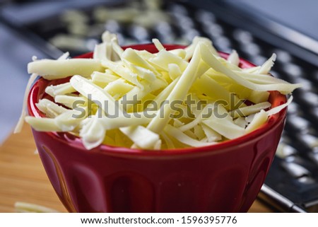 Grated Monterrey Jack cheese in red ceramic bowl. 