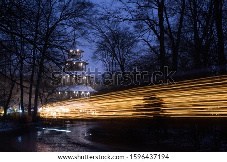 A horse cart drives in front of the Chinesischer Turm, or chinese tower, in the english garden in Munich, Germany, leaving a light streak at dusk.