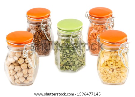 The collection of different groats in the glass jars isolated on white background. Split peas, buckwheat, chickpea and colorful lentils.