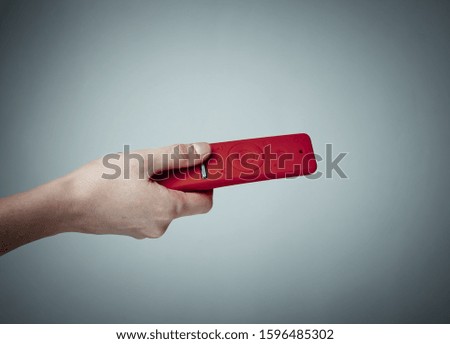 Female hand holds modern tv remote in red silicone case on gray background