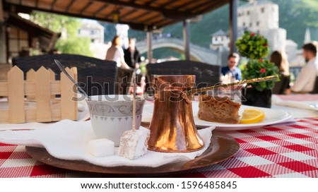 Traditional Bosnian coffee on the table with the view of Mostar Old bridge in the background, Bosnia and Herzegovina.  Traditional turkish coffee and turkish delight.  Royalty-Free Stock Photo #1596485845