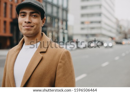 Side picture of handsome egyptian or arabian man stand on road alone and pose on camera. Wear stylish clothes. Alone outside. Daylight. Modern buildings behind. Urban view