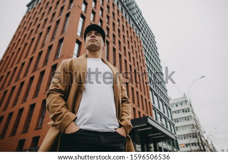 Calm peaceful confident arabian or egyptian man stand at street corner. Hold hands in pants pockets and look forward. Orange urban building behind. Daylight. Chilly weather. Stylish outfit